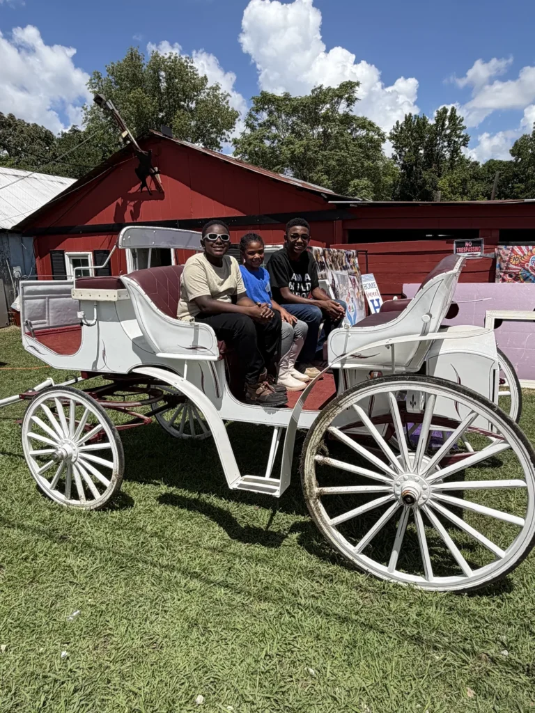 Three children smile from a white horse-drawn carriage at the Back to School Carnival