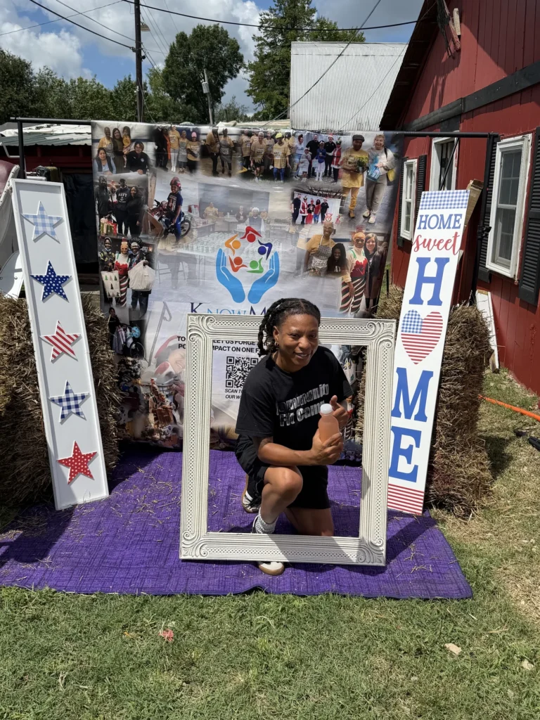 A Community Fit Camp volunteer kneels inside the photo frame in front of the Know More Tears banner