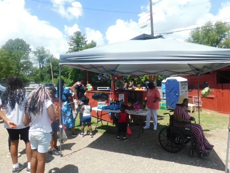 Families browse vendor tables under a white canopy beside the red barn
