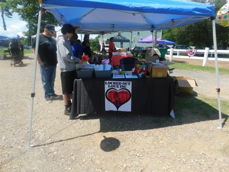 Visitors stop at the Locked Out Love Inc. table under a blue canopy