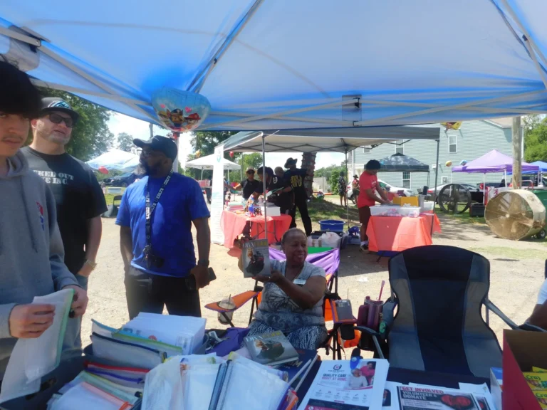 Volunteers talk with a guest at a resource table stacked with folders and handouts