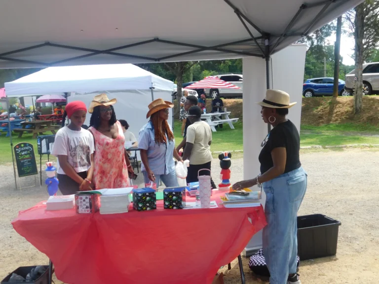 Guests in sun hats visit a vendor table under a canopy