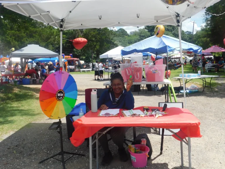 A volunteer staffs a prize wheel at a red-draped table