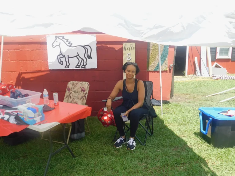 A volunteer waits at a vendor table beside the red barn