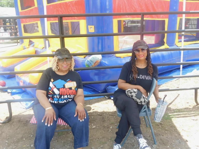 Two volunteers take a break on a bench beside the bounce house