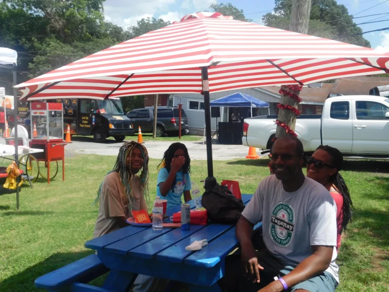 A family sits together at a picnic table in the shade